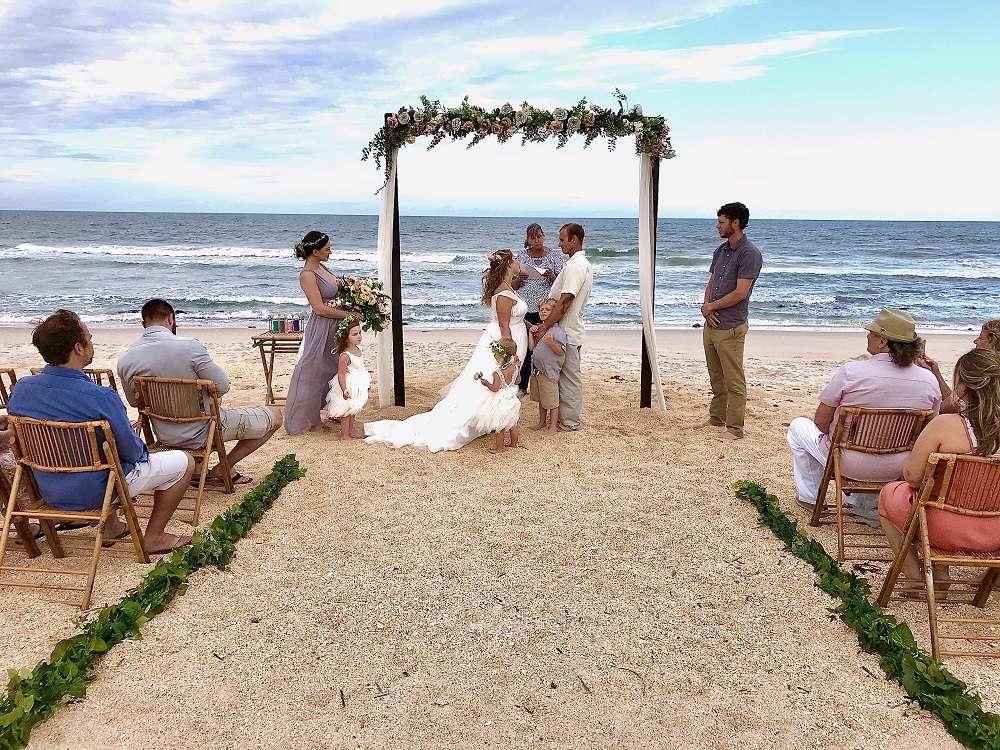 A beach wedding ceremony framed by flowers beside the ocean